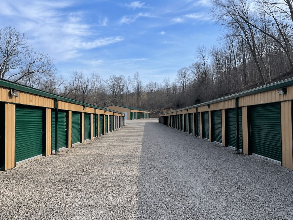 Wide gravel aisle running between two long rows of green-door storage units at U.S. 60 West Storage LLC